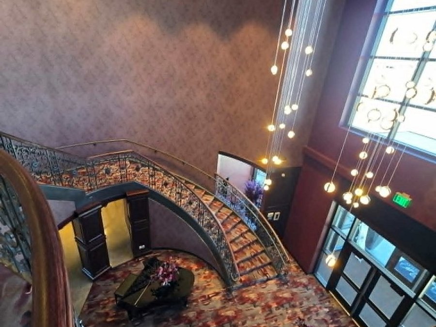 Finished hotel lobby with a curved staircase, grand piano and cascading pendant lights
