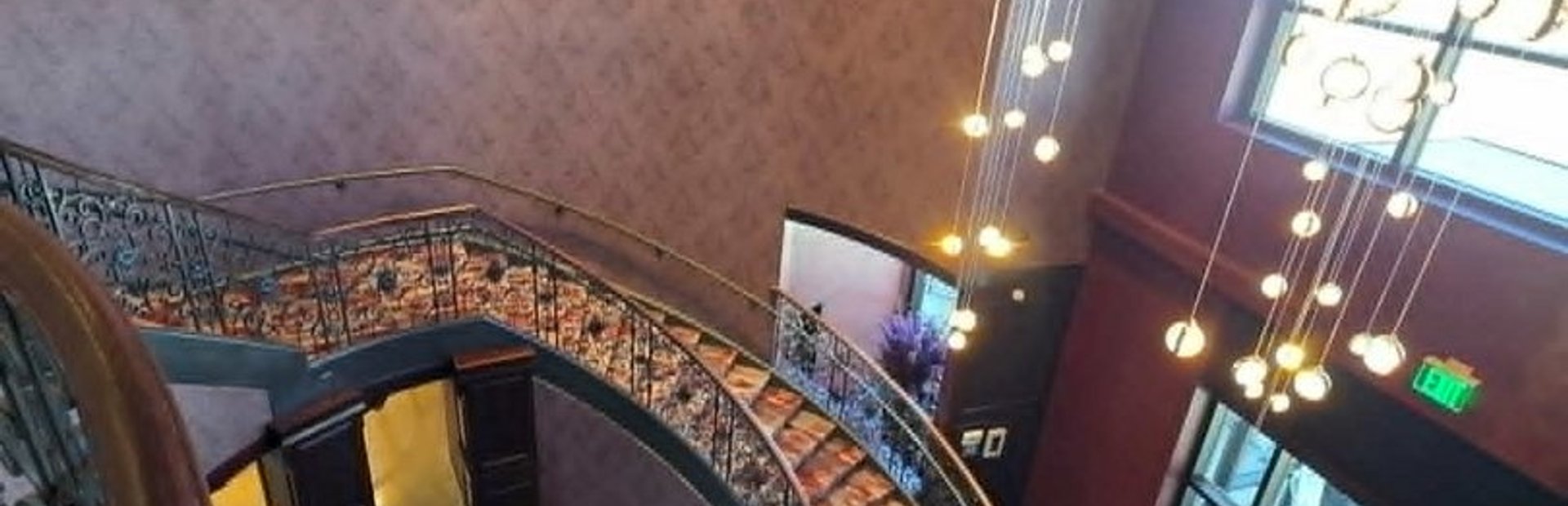 Finished hotel lobby with a curved staircase, grand piano and cascading pendant lights
