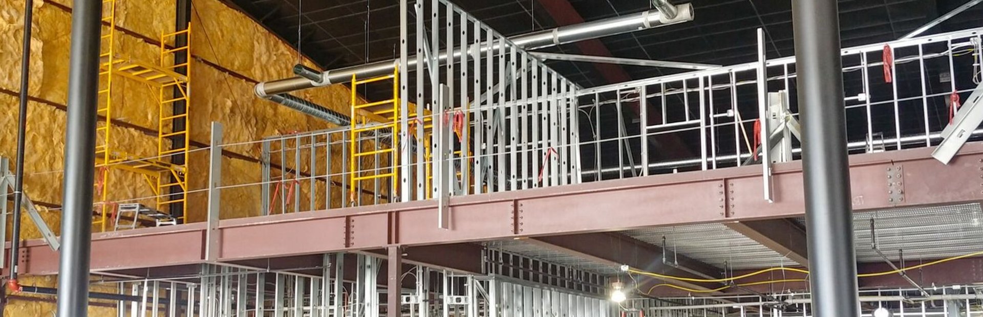 Active jobsite showing mezzanine steel framing, batt insulation and ductwork before ceiling grid is hung