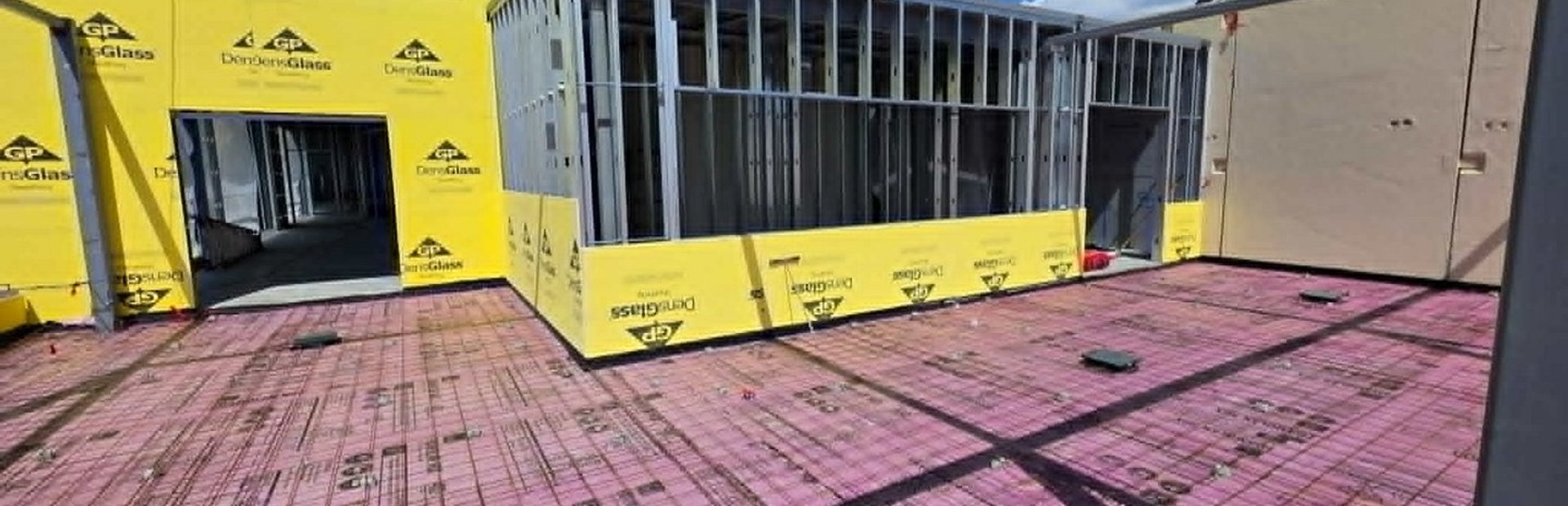 Rooftop metal stud framing with yellow DensGlass sheathing and rigid insulation board on a Labor House job